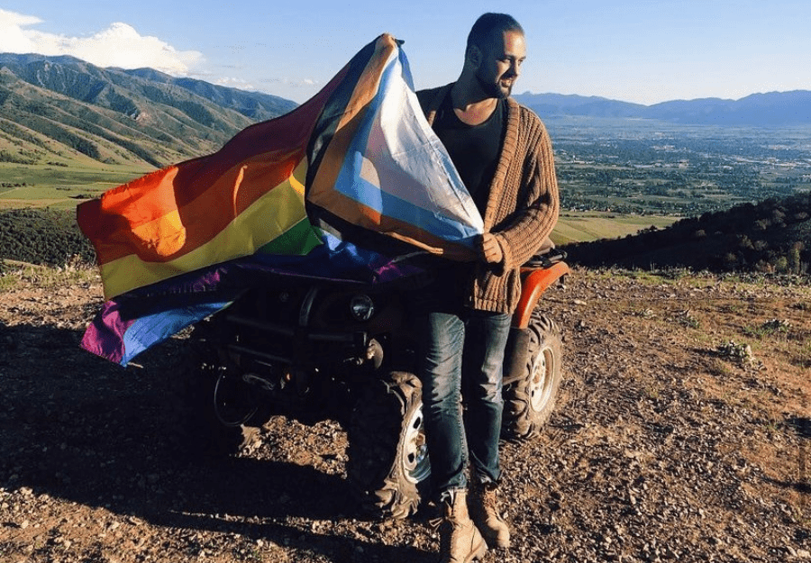 Person displaying the Progress Pride Flag on top of an ATV in a mountain landscape