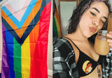 The Progress Pride Flag hanging on a bedroom wall next to a person holding a drink — lifestyle photo showing flag as home decor