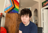 Customer with the Progress Pride Flag hanging on the wall behind them at home
