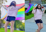 Person carrying the Progress Pride Flag draped around their shoulders like a cape, walking outdoors